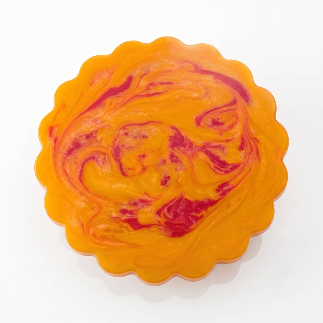 A scalloped circular dish or tray with a marbled swirl pattern of bright orange and deep red, photographed on a clean white background.
