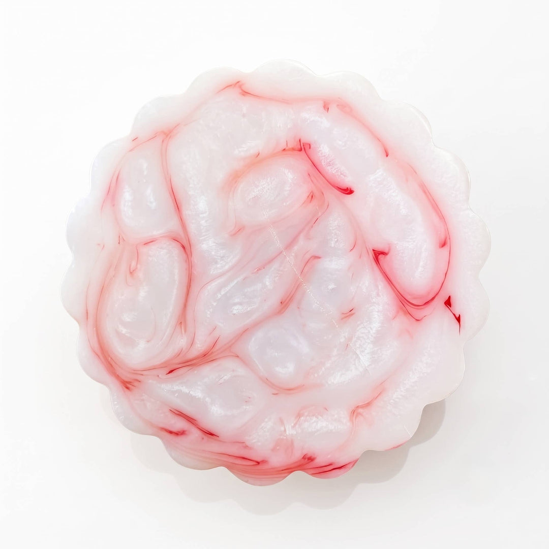 A round, scalloped-edge wax melt or soap bar with a glossy, brain-like marbled pattern in white and pink, set against a plain white background.