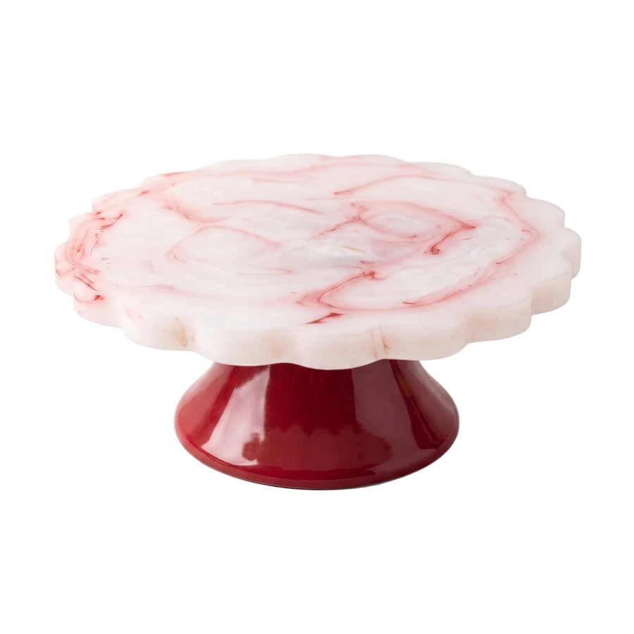 A pedestal cake stand with a scalloped white and pink marble top and a glossy deep red base, shown on a clean white background.