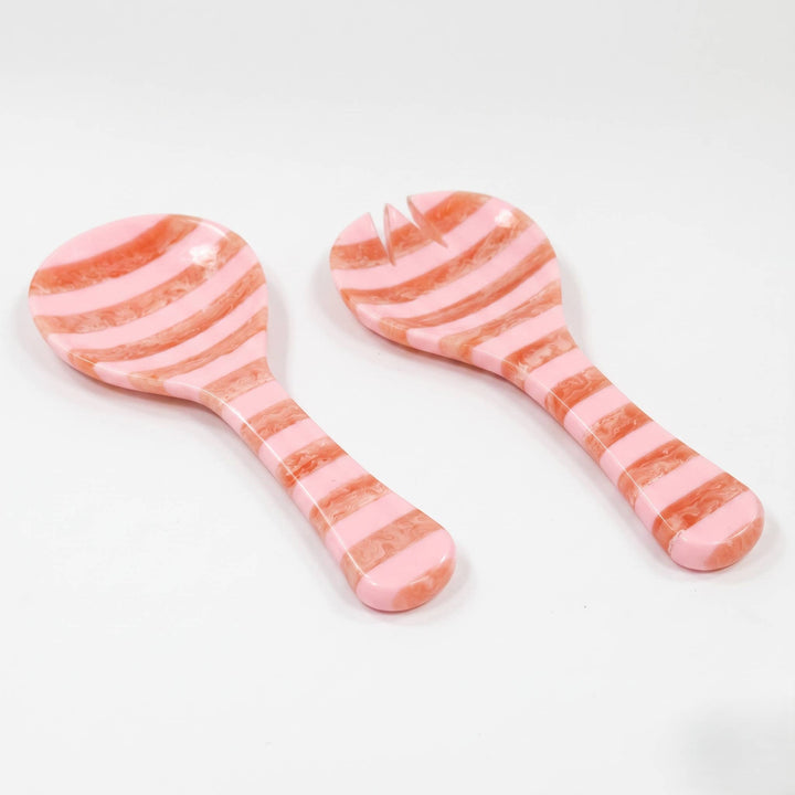 Two pink and peach striped serving utensils, one spoon and one small server with a fork head, on a white background.