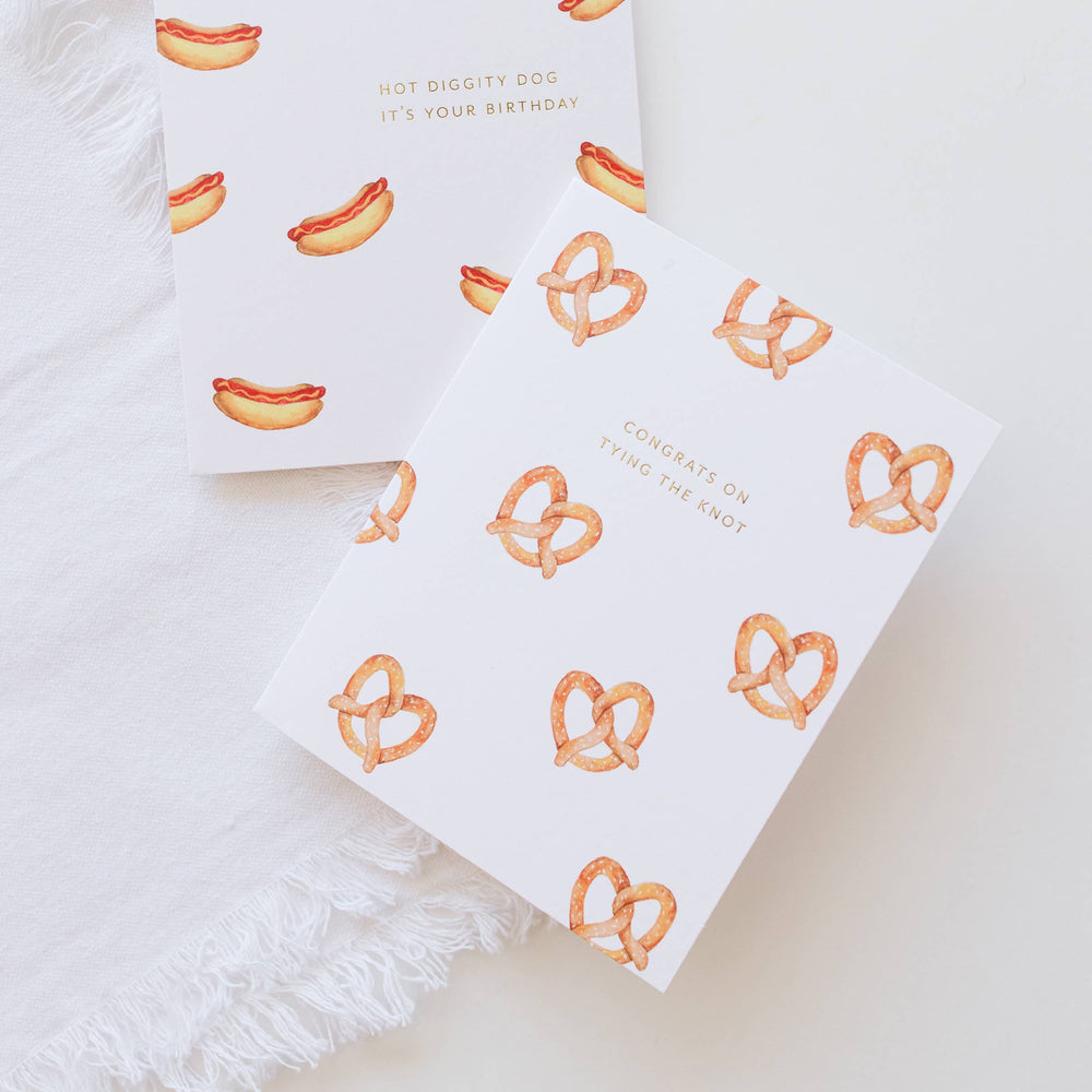 Two greeting cards with hot dog and pretzel designs on a white surface.