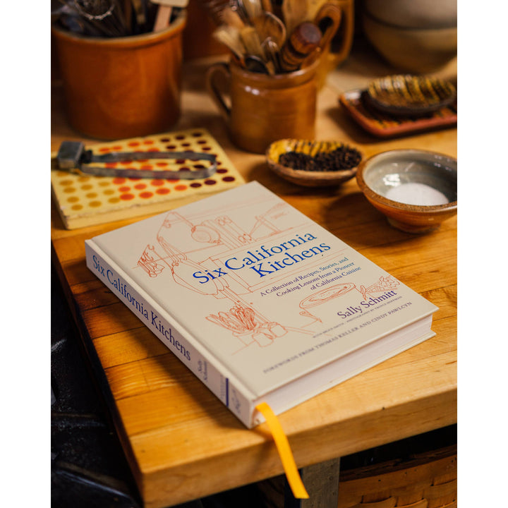 Book titled 'Six California Kitchens' on a wooden table with kitchen items in the background