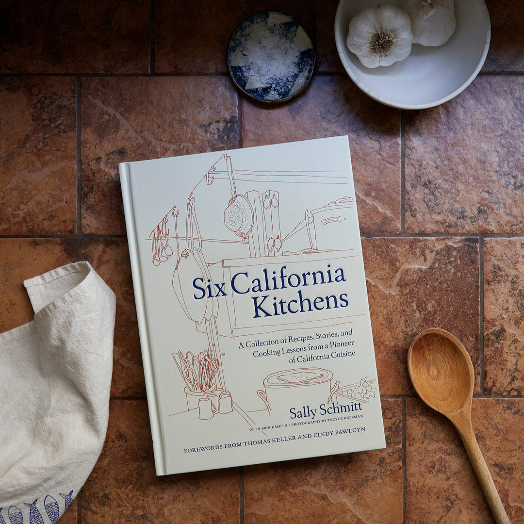 Book titled 'Six California Kitchens' by Sally Schmitt on a kitchen counter with a wooden spoon and garlic.