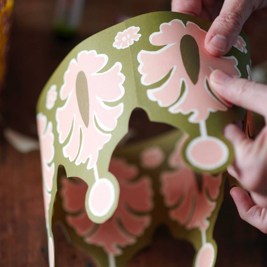 Hand holding a decorative paper cutout crown with floral patterns.