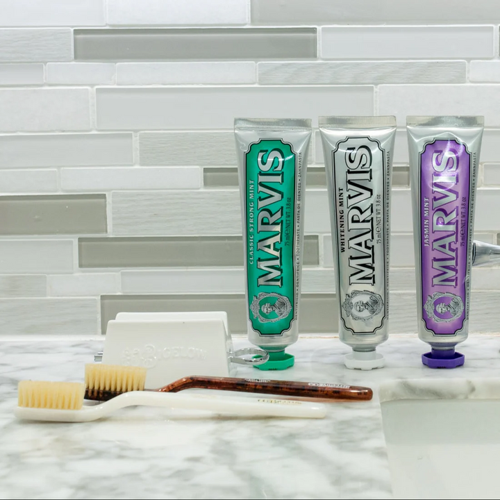 A lineup of marvis toothpaste with two toothbrushes and a toothpaste tube roller that squeezes out the last bits