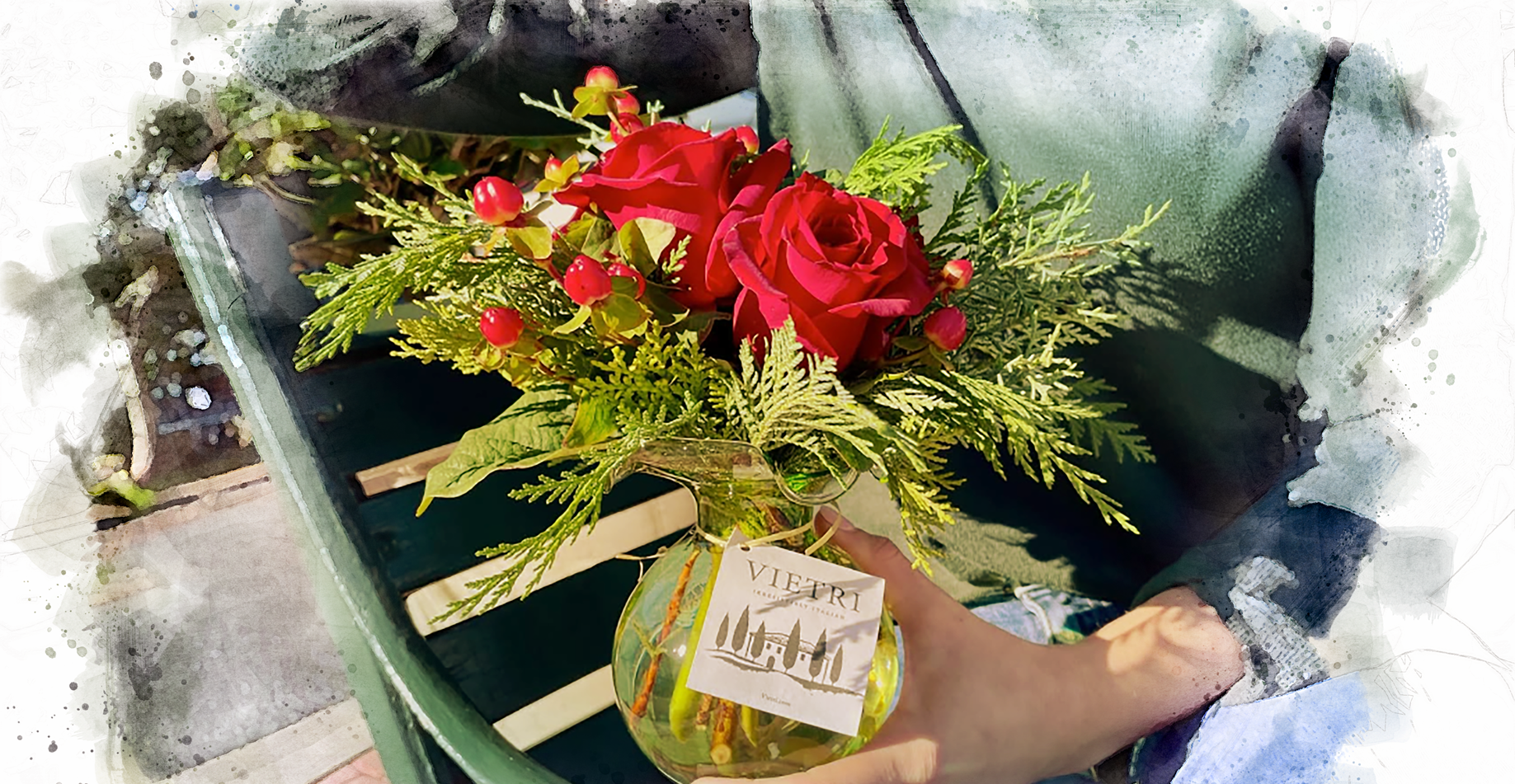 Bouquet of red roses and winter greenery in a glass vase held by a floral designer in a green sweater
